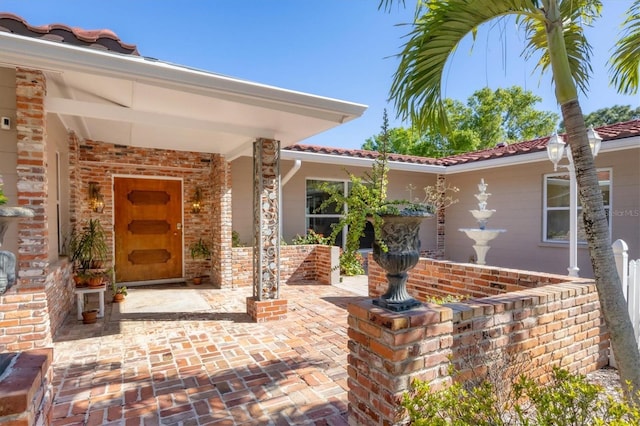 view of exterior entry with brick siding and a tiled roof