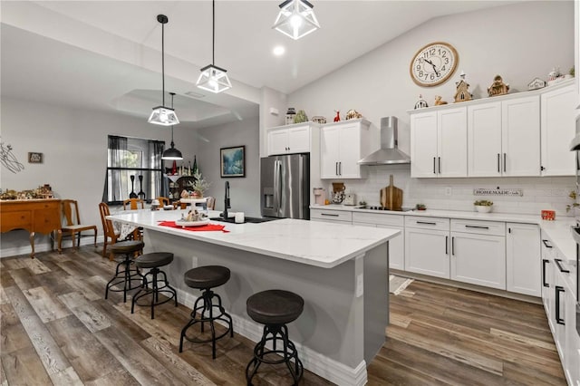 kitchen with a center island, wall chimney exhaust hood, stainless steel fridge, and white cabinets