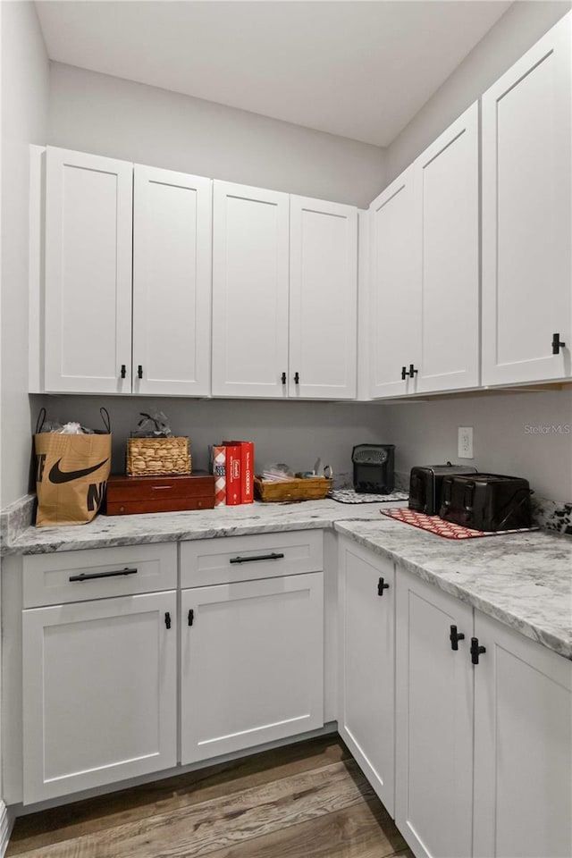 kitchen featuring white cabinets, light stone counters, and dark wood-type flooring