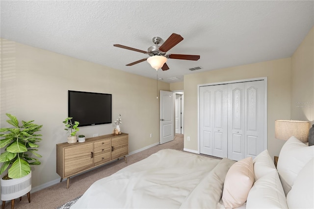 bedroom with light carpet, a closet, ceiling fan, and a textured ceiling