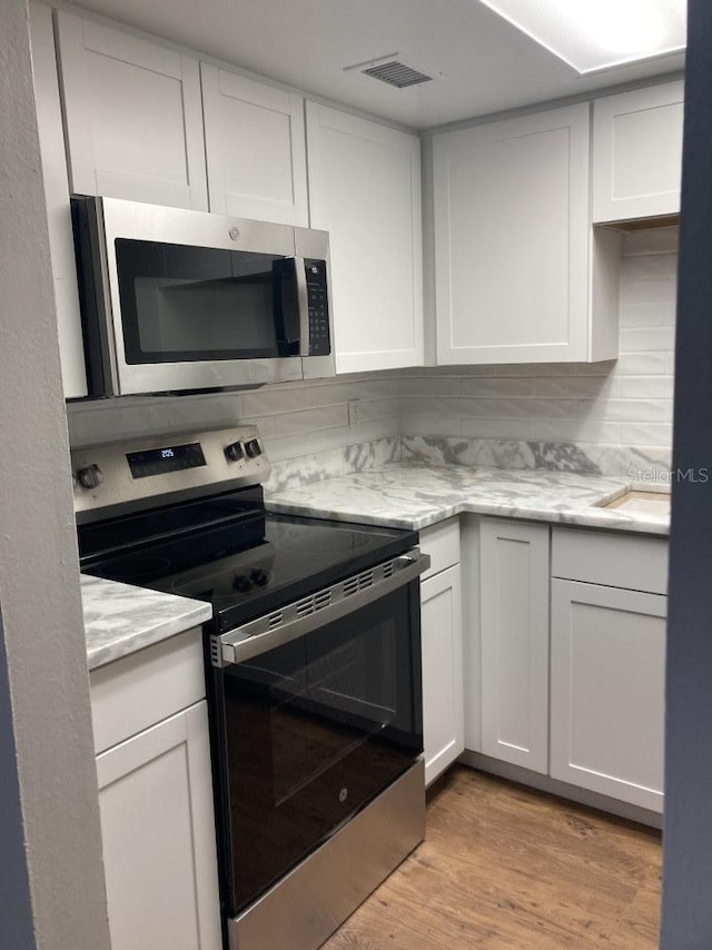 kitchen with stainless steel appliances, white cabinetry, and light hardwood / wood-style flooring