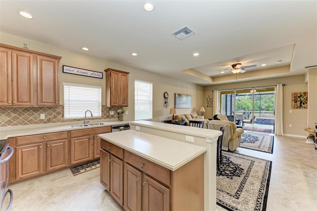 kitchen with tasteful backsplash, a raised ceiling, ceiling fan, sink, and a center island