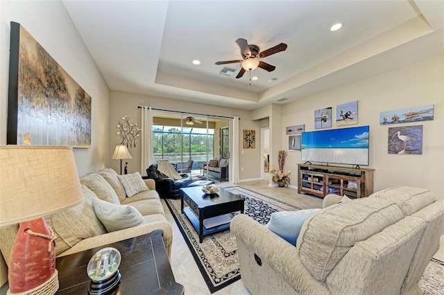 tiled living room with ceiling fan and a tray ceiling