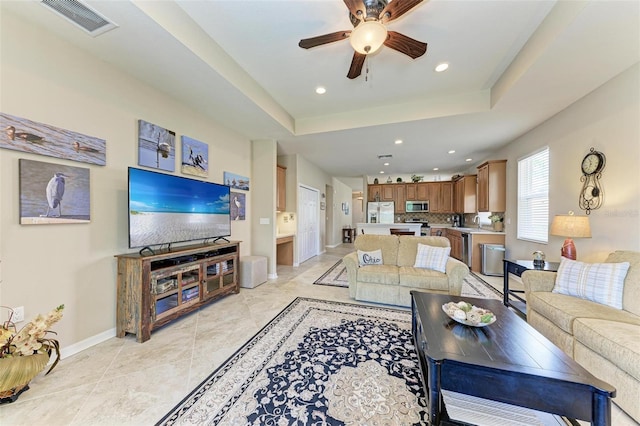 living room with a tray ceiling, ceiling fan, and sink