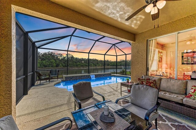 pool at dusk with glass enclosure, a patio area, a water view, and ceiling fan