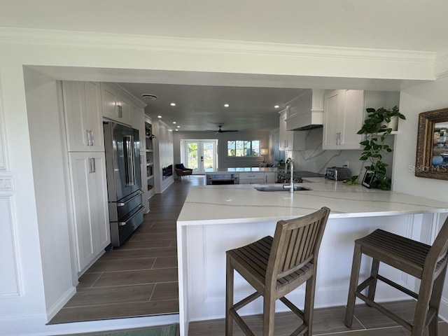 kitchen with white cabinetry, premium range hood, kitchen peninsula, a kitchen bar, and high end fridge