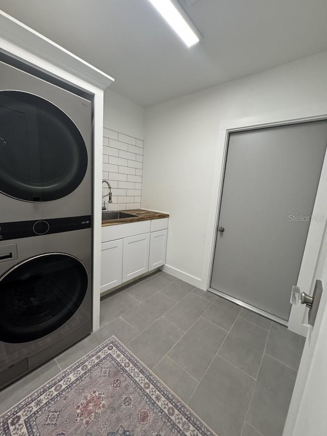 clothes washing area with stacked washer / dryer, sink, light tile patterned flooring, and cabinets