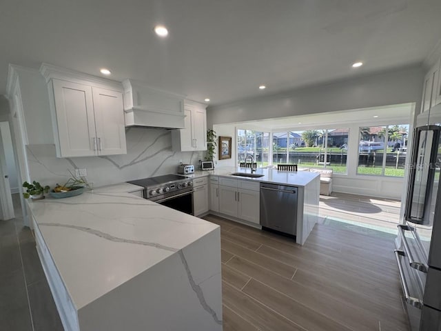 kitchen with white cabinets, sink, light stone countertops, appliances with stainless steel finishes, and kitchen peninsula