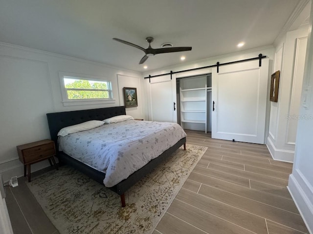 bedroom featuring a barn door, ceiling fan, a closet, and ornamental molding