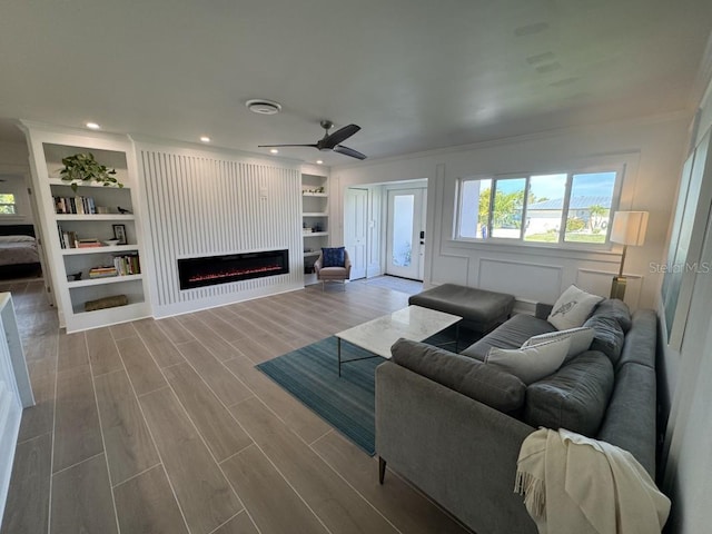 living room featuring ceiling fan, built in features, crown molding, and hardwood / wood-style flooring