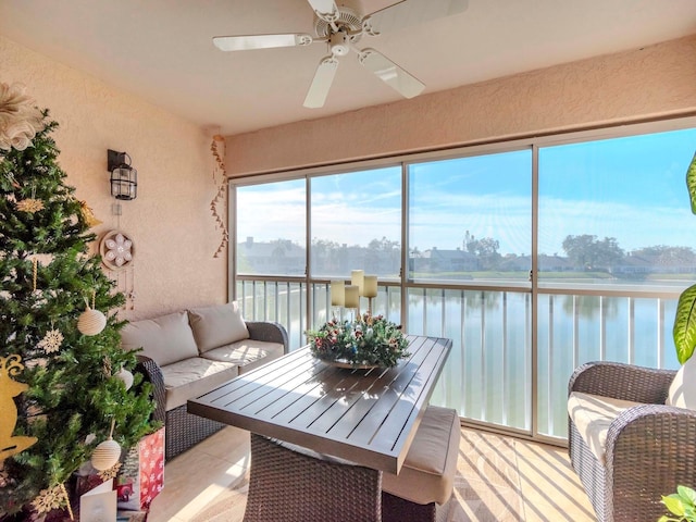 sunroom with ceiling fan and a water view