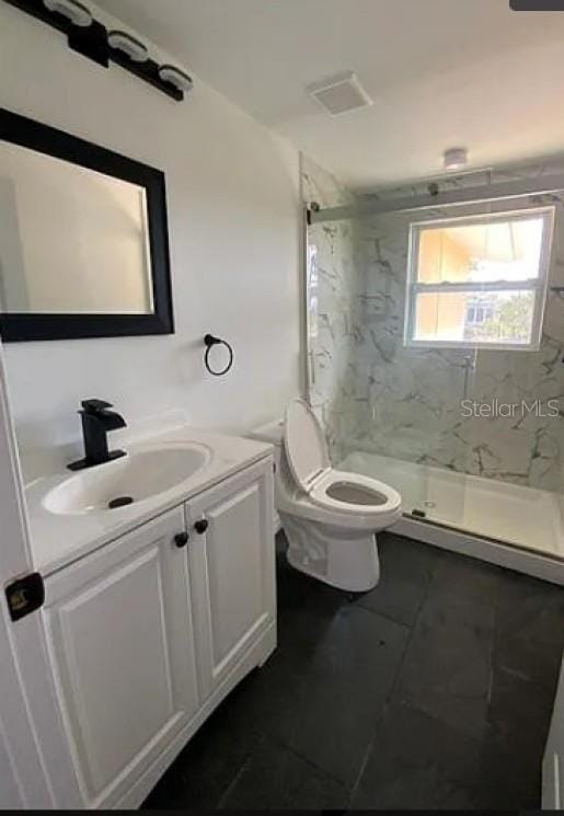 bathroom with tile patterned flooring, vanity, toilet, and a tile shower