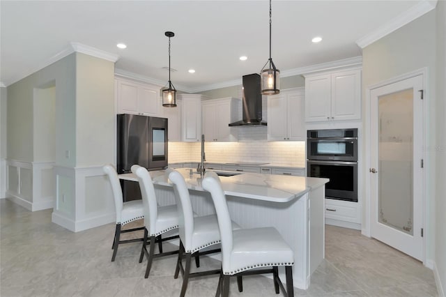 kitchen with hanging light fixtures, an island with sink, wall chimney range hood, stainless steel fridge, and white cabinets