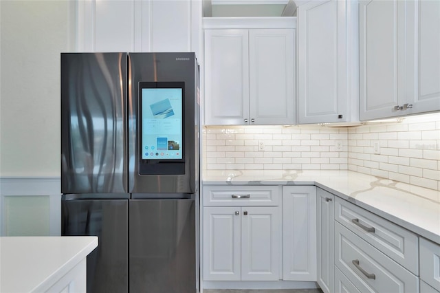 kitchen with white cabinets, stainless steel fridge, light stone countertops, and decorative backsplash