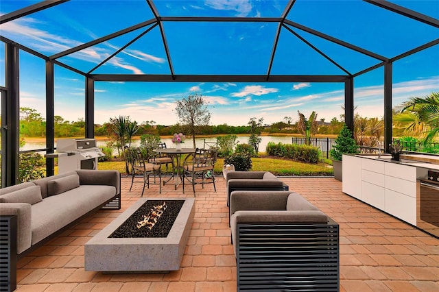 view of patio with a lanai, an outdoor living space with a fire pit, and a water view