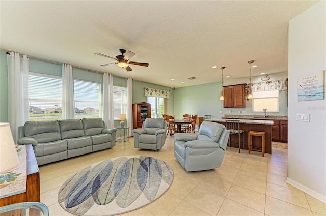 living room with a textured ceiling, ceiling fan, light tile patterned flooring, and sink