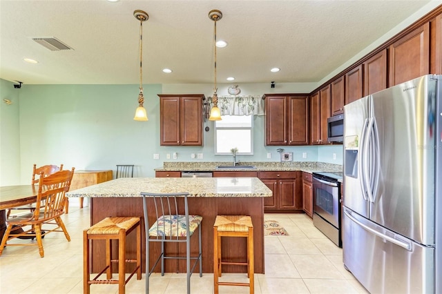 kitchen featuring light stone countertops, sink, hanging light fixtures, stainless steel appliances, and a kitchen island