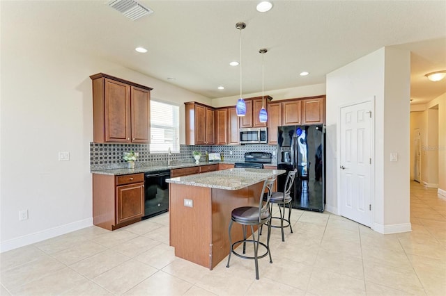 kitchen featuring a breakfast bar, a center island, black appliances, hanging light fixtures, and light stone countertops