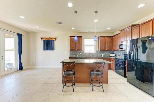 kitchen with pendant lighting, a center island, dark stone counters, black appliances, and a kitchen bar