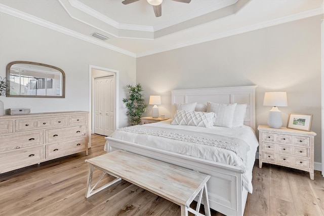 bedroom with crown molding, light hardwood / wood-style flooring, ceiling fan, a tray ceiling, and a closet