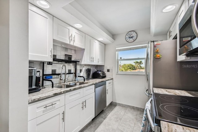 kitchen with white cabinets, appliances with stainless steel finishes, light stone countertops, and sink