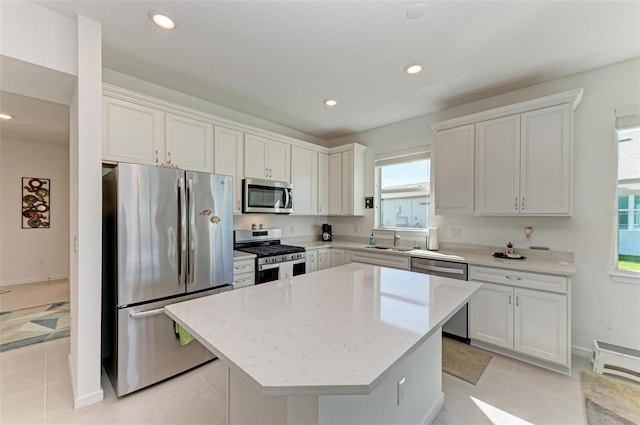 kitchen with light stone countertops, light tile patterned floors, a kitchen island, white cabinetry, and stainless steel appliances