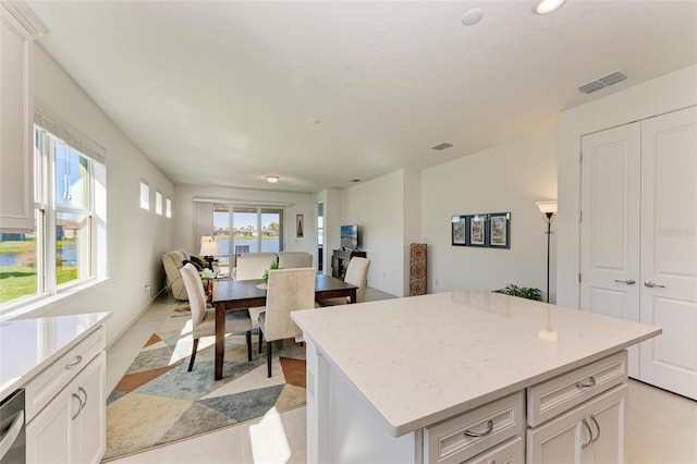 kitchen with dishwasher, a center island, white cabinets, and light stone counters