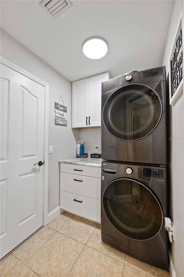 washroom with stacked washer / drying machine, light tile patterned flooring, and cabinets