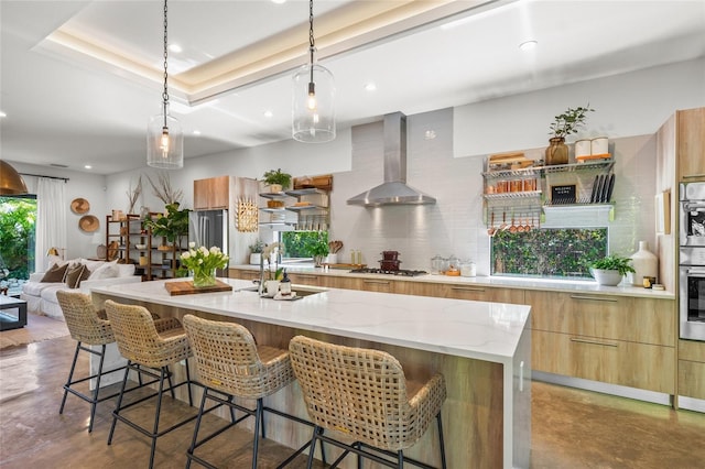 kitchen featuring wall chimney exhaust hood, a breakfast bar, stainless steel appliances, concrete floors, and a large island