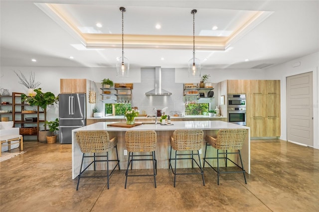 kitchen with a center island with sink, a kitchen breakfast bar, wall chimney range hood, appliances with stainless steel finishes, and decorative light fixtures