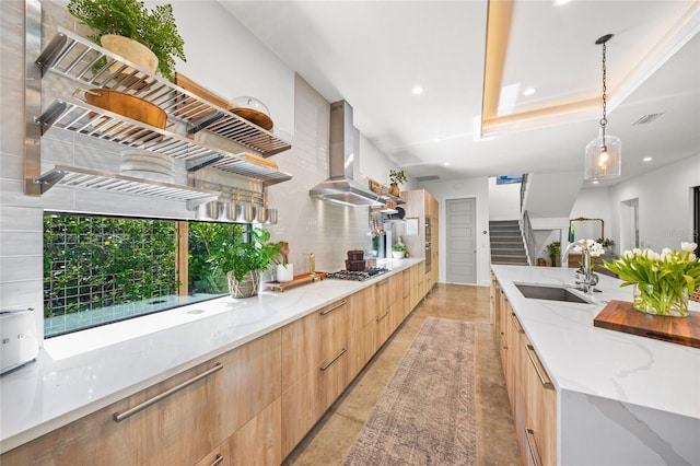 kitchen with light stone countertops, sink, hanging light fixtures, stainless steel gas cooktop, and extractor fan