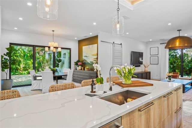 kitchen featuring a barn door, light stone counters, sink, and pendant lighting