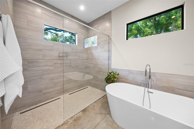 bathroom featuring plus walk in shower, tile patterned flooring, plenty of natural light, and tile walls