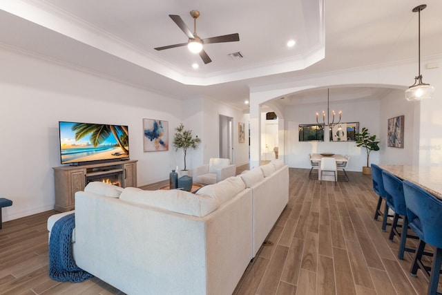 living room with a tray ceiling, crown molding, ceiling fan with notable chandelier, and hardwood / wood-style flooring