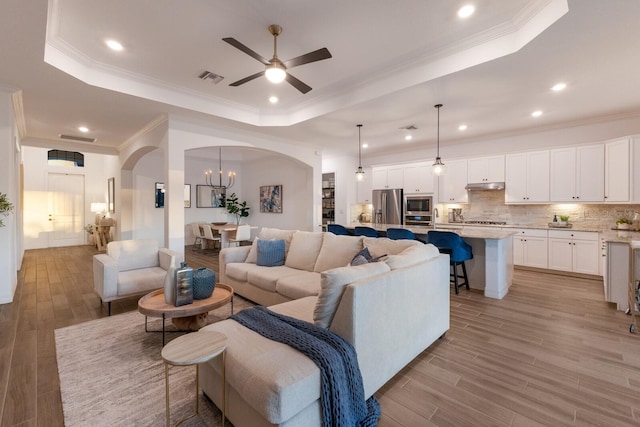 living room featuring a raised ceiling, ornamental molding, and light wood-type flooring