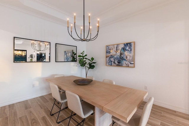 dining space featuring a raised ceiling, light hardwood / wood-style flooring, a notable chandelier, and crown molding