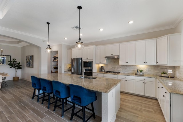 kitchen featuring white cabinets, appliances with stainless steel finishes, decorative light fixtures, and an island with sink