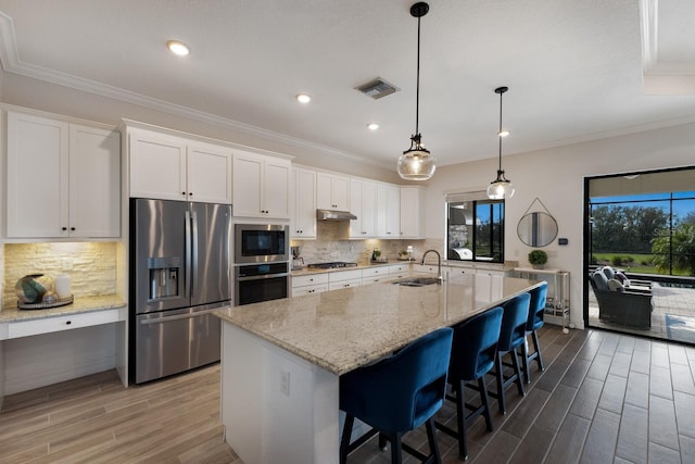 kitchen featuring white cabinetry, stainless steel appliances, light stone counters, a breakfast bar area, and a center island with sink