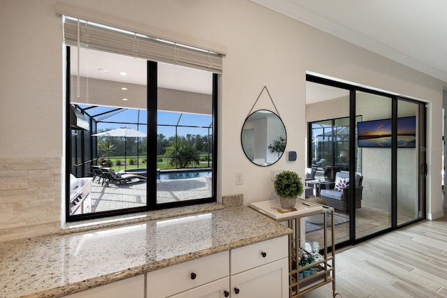 kitchen with white cabinets, light wood-type flooring, light stone countertops, and ornamental molding