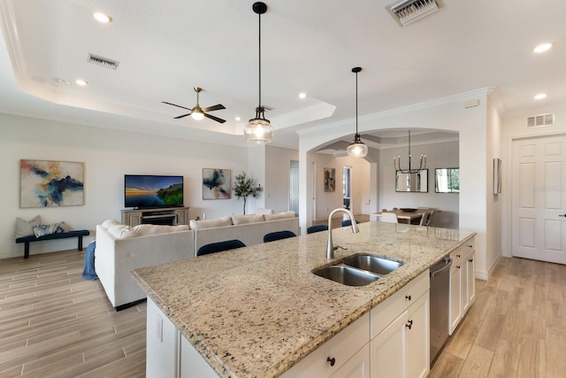 kitchen with decorative light fixtures, white cabinetry, sink, and a kitchen island with sink