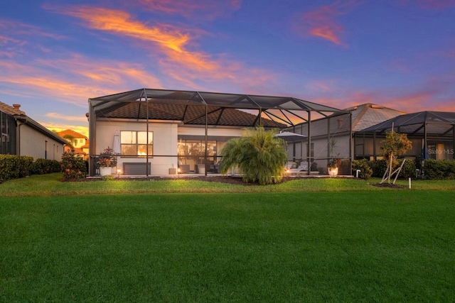 back house at dusk with glass enclosure and a lawn