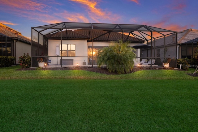 back house at dusk with a lawn and glass enclosure