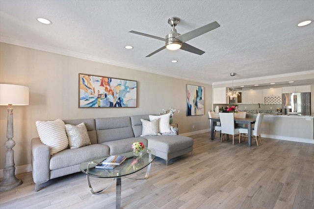 living room with a textured ceiling, ceiling fan with notable chandelier, light hardwood / wood-style floors, and crown molding