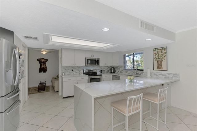 kitchen with sink, stainless steel appliances, kitchen peninsula, a breakfast bar area, and white cabinets