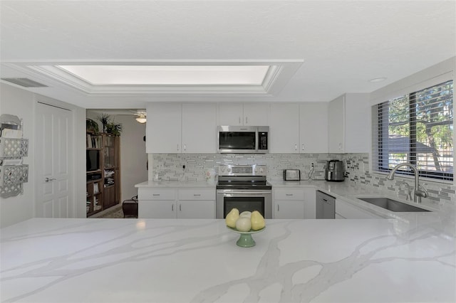 kitchen with a skylight, white cabinetry, sink, light stone counters, and appliances with stainless steel finishes