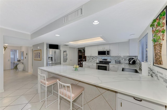 kitchen with a kitchen bar, appliances with stainless steel finishes, backsplash, kitchen peninsula, and white cabinets