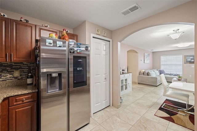 kitchen with decorative backsplash, stainless steel refrigerator with ice dispenser, stone countertops, and light tile patterned flooring