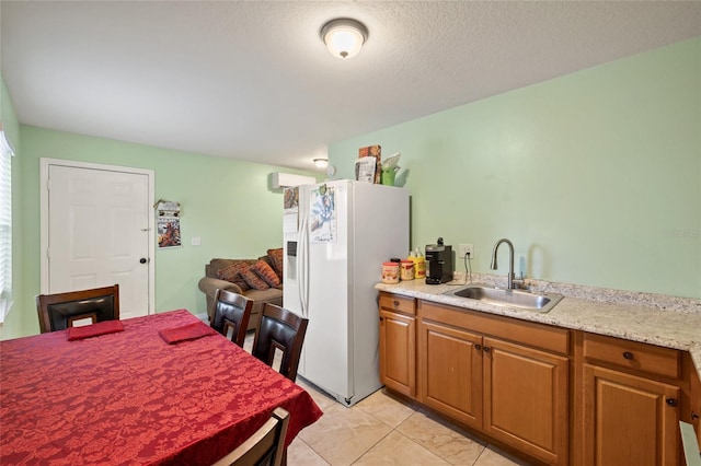 kitchen featuring sink, white fridge with ice dispenser, a textured ceiling, light tile patterned flooring, and light stone counters