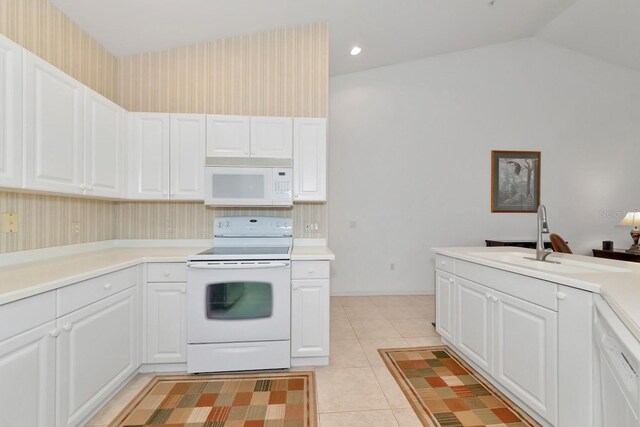 kitchen with lofted ceiling, white appliances, sink, light tile patterned floors, and white cabinetry