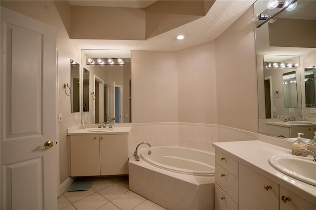 bathroom with tile patterned flooring, vanity, a textured ceiling, and tiled tub